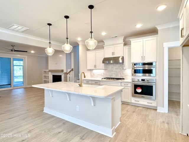 kitchen featuring a kitchen bar, under cabinet range hood, a sink, light wood-style flooring, and stainless steel appliances