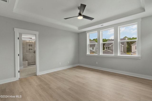 unfurnished bedroom featuring connected bathroom, a tray ceiling, light hardwood / wood-style floors, and ceiling fan