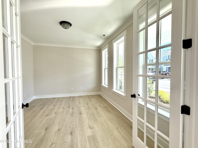 spare room featuring baseboards, ornamental molding, and light wood finished floors