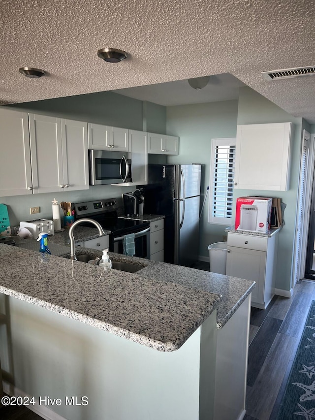 kitchen featuring kitchen peninsula, appliances with stainless steel finishes, light stone countertops, dark hardwood / wood-style floors, and white cabinetry