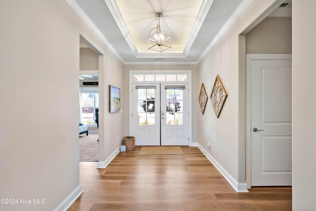 foyer entrance with french doors, a raised ceiling, crown molding, a chandelier, and wood-type flooring