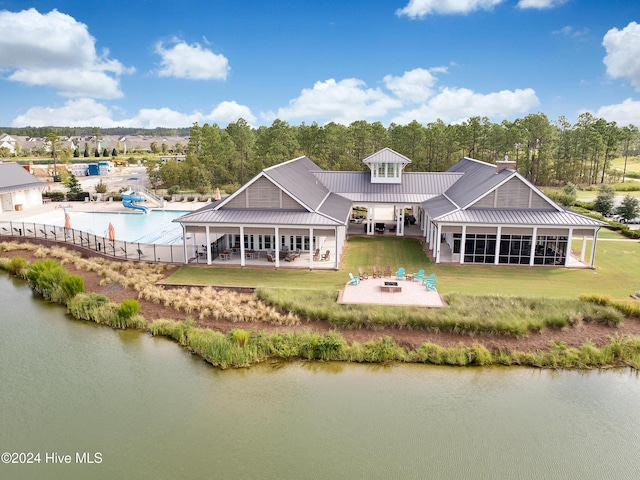 rear view of property featuring a lawn, a sunroom, a fire pit, a patio area, and a water view