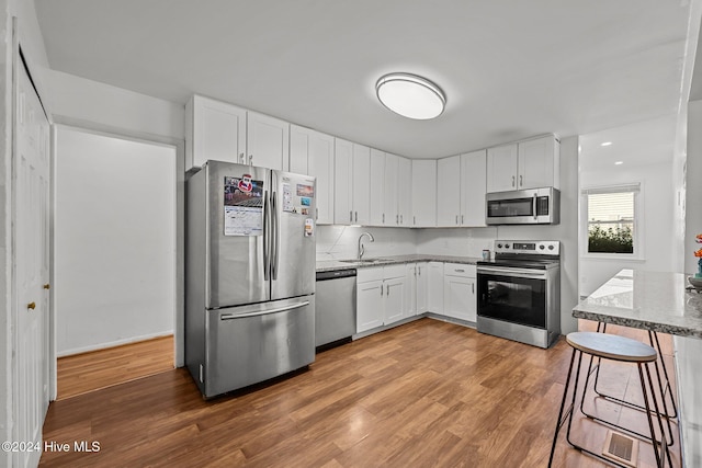 kitchen featuring stone counters, hardwood / wood-style floors, white cabinets, and appliances with stainless steel finishes