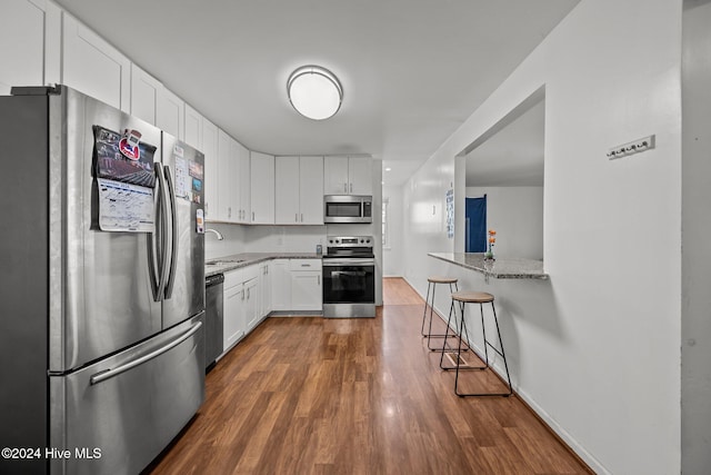 kitchen with a breakfast bar, white cabinets, dark hardwood / wood-style floors, light stone countertops, and stainless steel appliances