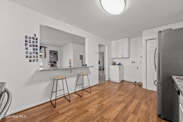 kitchen with light stone counters, white cabinets, light wood-type flooring, and appliances with stainless steel finishes