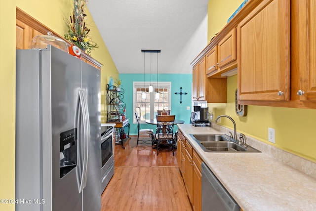 kitchen featuring hanging light fixtures, sink, vaulted ceiling, light hardwood / wood-style flooring, and appliances with stainless steel finishes