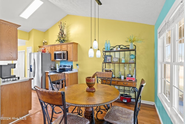 dining space featuring a healthy amount of sunlight, lofted ceiling, and light hardwood / wood-style flooring