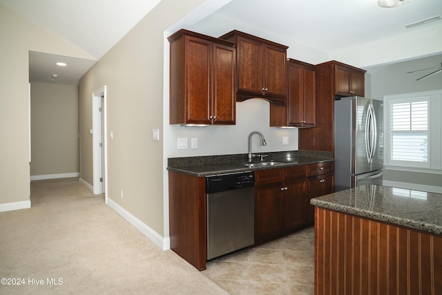 kitchen with appliances with stainless steel finishes, dark stone counters, light colored carpet, vaulted ceiling, and sink