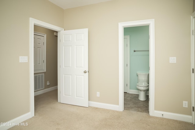 unfurnished bedroom featuring a walk in closet, ensuite bathroom, and light colored carpet