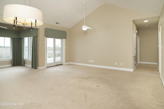 carpeted empty room featuring high vaulted ceiling, a healthy amount of sunlight, and ceiling fan with notable chandelier