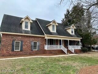 new england style home with a front yard, covered porch, and brick siding