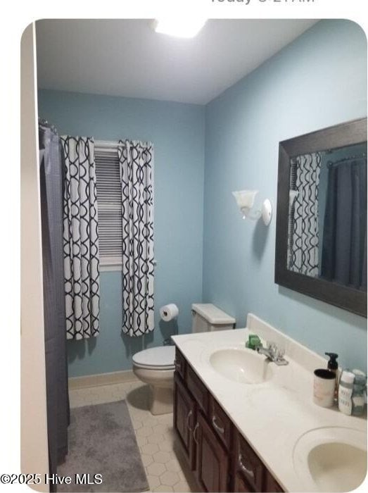 bathroom with a sink, tile patterned floors, toilet, and double vanity