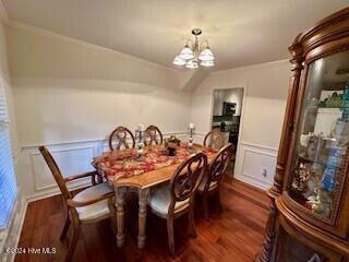 dining area featuring dark wood-style flooring, a wainscoted wall, a chandelier, and a decorative wall