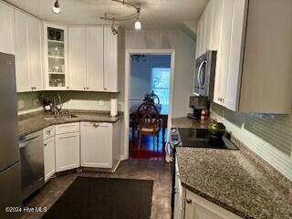 kitchen with appliances with stainless steel finishes, a sink, decorative light fixtures, white cabinetry, and glass insert cabinets