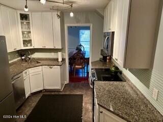 kitchen featuring dark stone countertops, hanging light fixtures, stainless steel appliances, white cabinetry, and glass insert cabinets