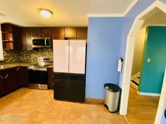 kitchen featuring appliances with stainless steel finishes, ornamental molding, backsplash, and dark brown cabinetry