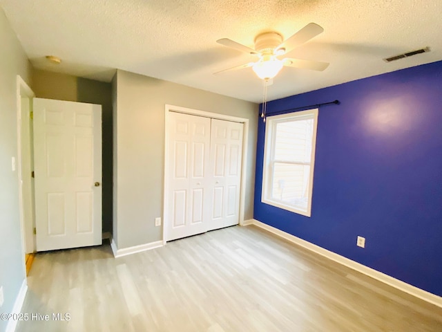 unfurnished bedroom with a textured ceiling, ceiling fan, a closet, and light wood-type flooring