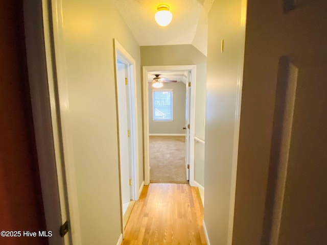 corridor with light wood-type flooring and vaulted ceiling