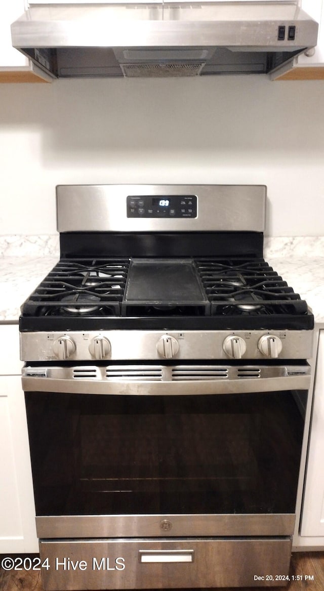 details with white cabinets, ventilation hood, light stone counters, and stainless steel range with gas stovetop