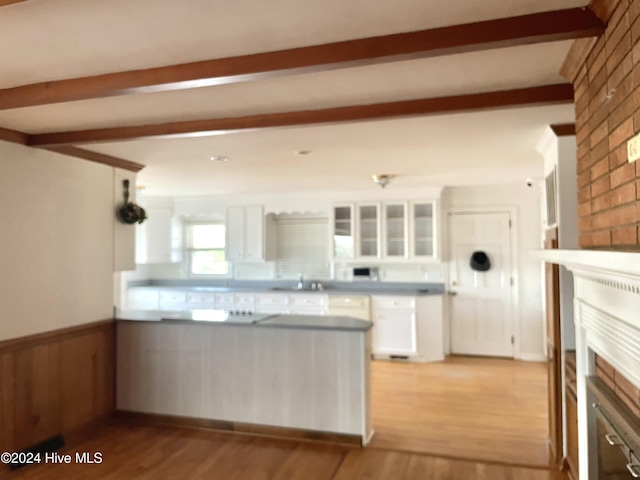 kitchen with white cabinets, light hardwood / wood-style floors, sink, a brick fireplace, and beam ceiling