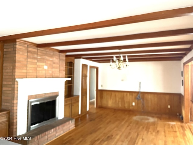 unfurnished living room with beam ceiling, a fireplace, an inviting chandelier, and hardwood / wood-style flooring