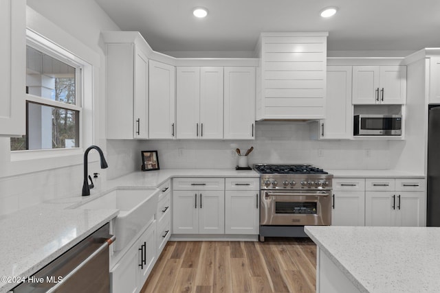 kitchen with appliances with stainless steel finishes, light hardwood / wood-style floors, white cabinetry, and sink