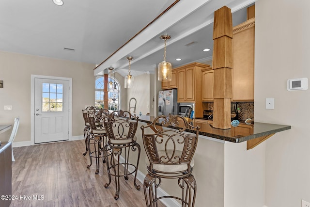 kitchen featuring a breakfast bar, stainless steel appliances, backsplash, light wood-style floors, and a peninsula