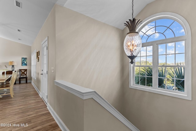 hallway with wood-type flooring, vaulted ceiling, and an inviting chandelier