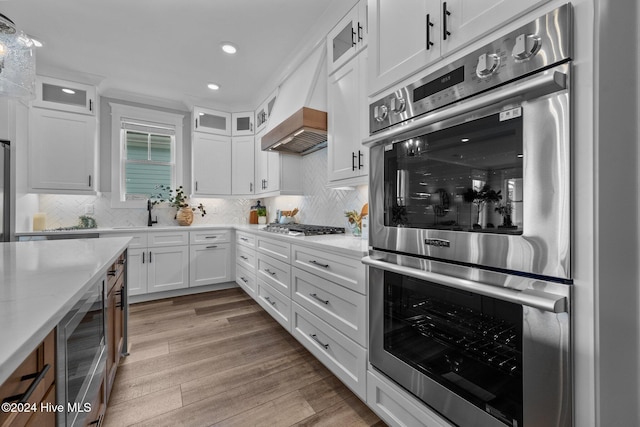 kitchen with tasteful backsplash, custom exhaust hood, stainless steel appliances, light hardwood / wood-style flooring, and white cabinets