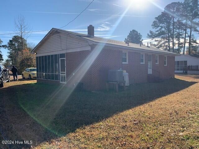 back of property with a sunroom, a yard, and cooling unit