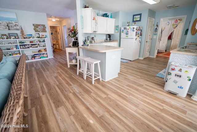 kitchen with white cabinetry, white appliances, light hardwood / wood-style flooring, and a breakfast bar