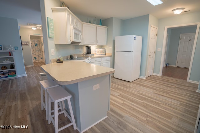 kitchen featuring white appliances, white cabinets, light wood-type flooring, kitchen peninsula, and a breakfast bar