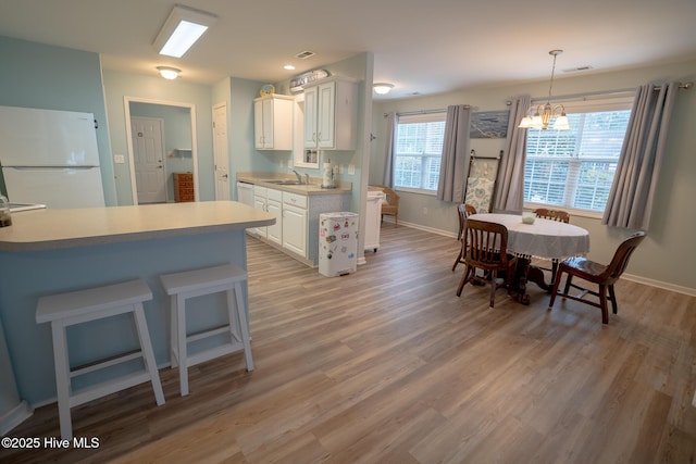 kitchen with hanging light fixtures, sink, light wood-type flooring, white cabinets, and white appliances