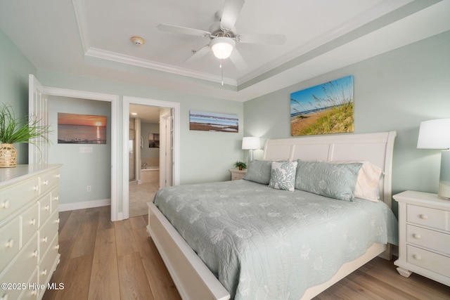 bedroom featuring baseboards, a raised ceiling, wood finished floors, and ensuite bath