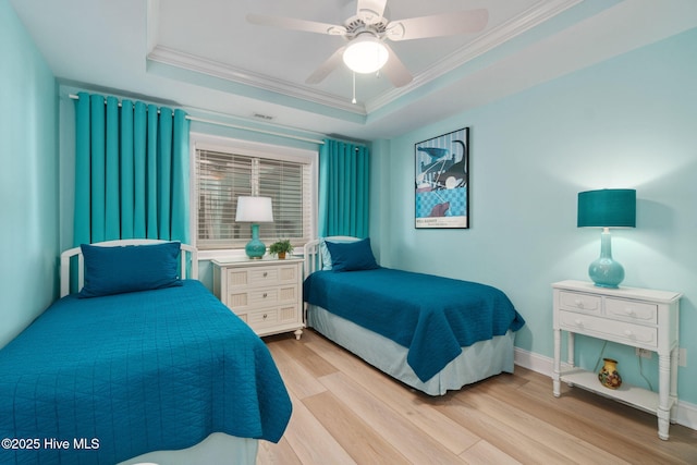 bedroom with baseboards, light wood-style floors, crown molding, and a tray ceiling