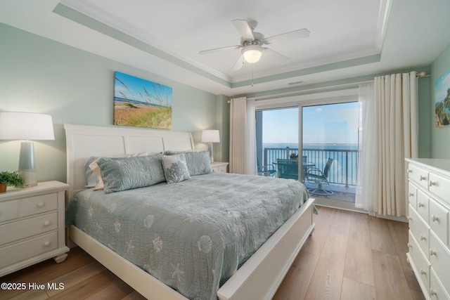 bedroom with light wood-type flooring, a tray ceiling, access to outside, and a water view