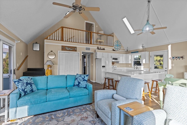 living room featuring a skylight, ceiling fan, sink, high vaulted ceiling, and hardwood / wood-style floors