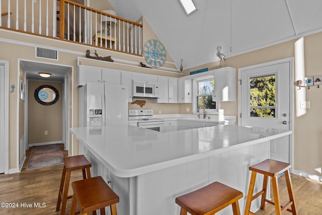 kitchen with a kitchen breakfast bar, high vaulted ceiling, dark hardwood / wood-style floors, white appliances, and white cabinets