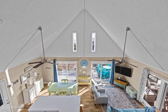 living room with ceiling fan, hardwood / wood-style floors, high vaulted ceiling, and a textured ceiling