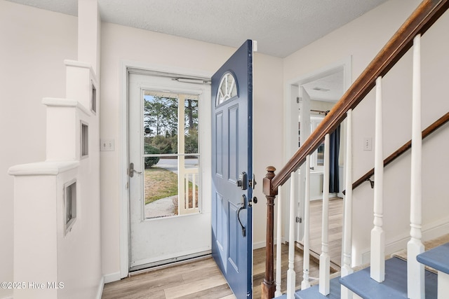 entrance foyer with light wood-style floors, stairs, and a textured ceiling