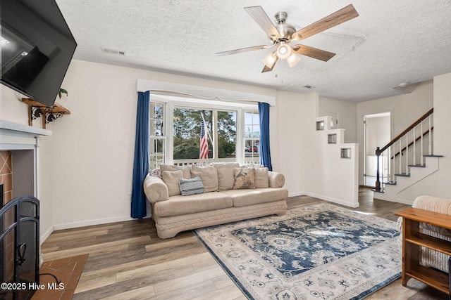 living area featuring stairway, visible vents, light wood-style flooring, a textured ceiling, and a tiled fireplace