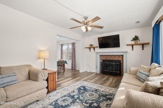 living area with visible vents, a textured ceiling, wood finished floors, ceiling fan, and a tile fireplace