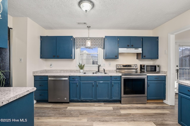 kitchen with under cabinet range hood, light wood-type flooring, appliances with stainless steel finishes, blue cabinets, and a sink