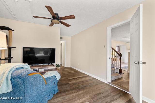 living room with a ceiling fan, wood finished floors, baseboards, attic access, and a textured ceiling