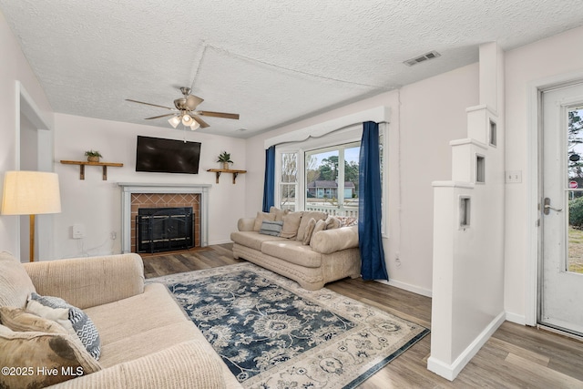 living room featuring visible vents, a ceiling fan, wood finished floors, a fireplace, and baseboards