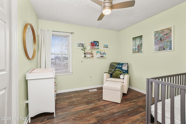 bedroom with a nursery area, wood finished floors, baseboards, and ceiling fan