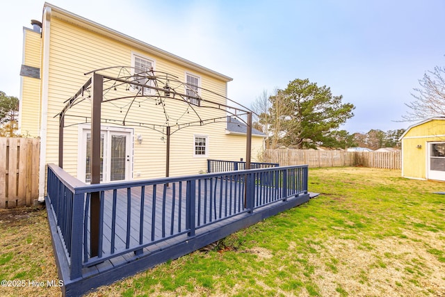 rear view of house featuring a deck, an outdoor structure, a fenced backyard, and a lawn