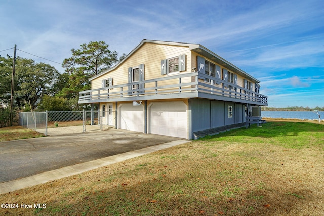 view of property exterior featuring a garage, a water view, fence, driveway, and a lawn