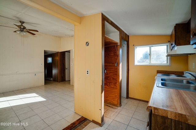 kitchen featuring ceiling fan, wooden walls, sink, and light tile patterned floors