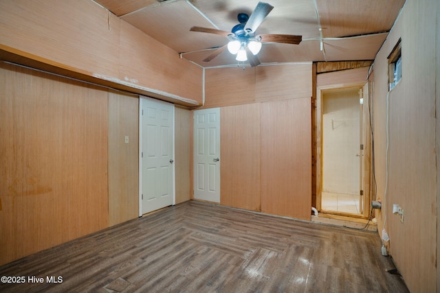 unfurnished bedroom featuring ceiling fan, hardwood / wood-style floors, vaulted ceiling, and wooden walls